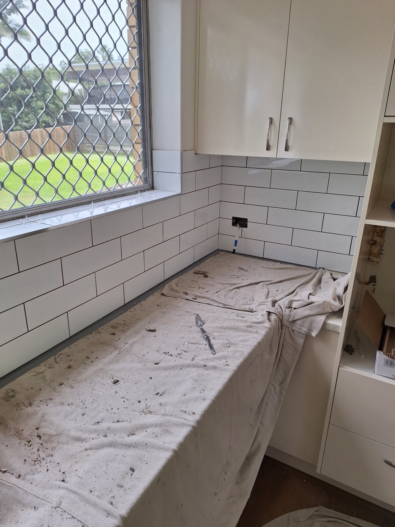 Kitchen splashback installation with white subway tiles and dark grout