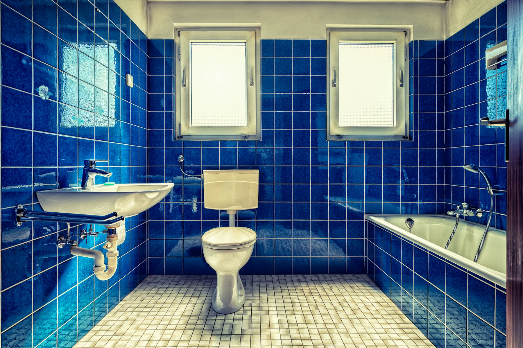 Blue tiled bathroom with sink, toilet and tiled floor